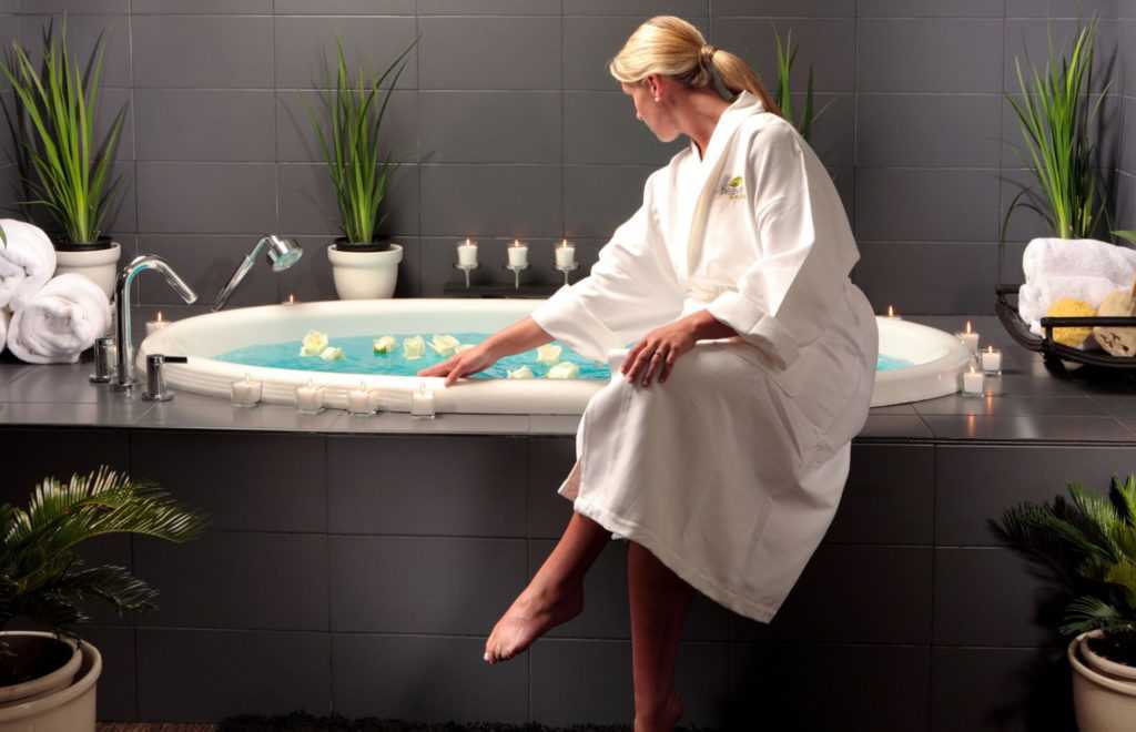 A woman in a robe sitting on the edge of a candlelit spa jacuzzi tub