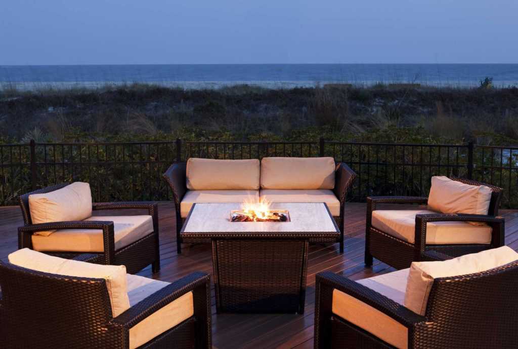 a bon fire on a patio next to the beach at dusk surrounded by chairs