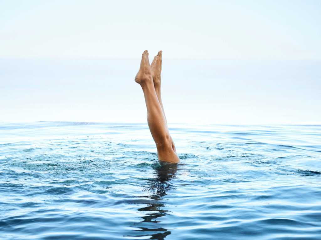 A swimmer with her legs sticking upright out of the blue water