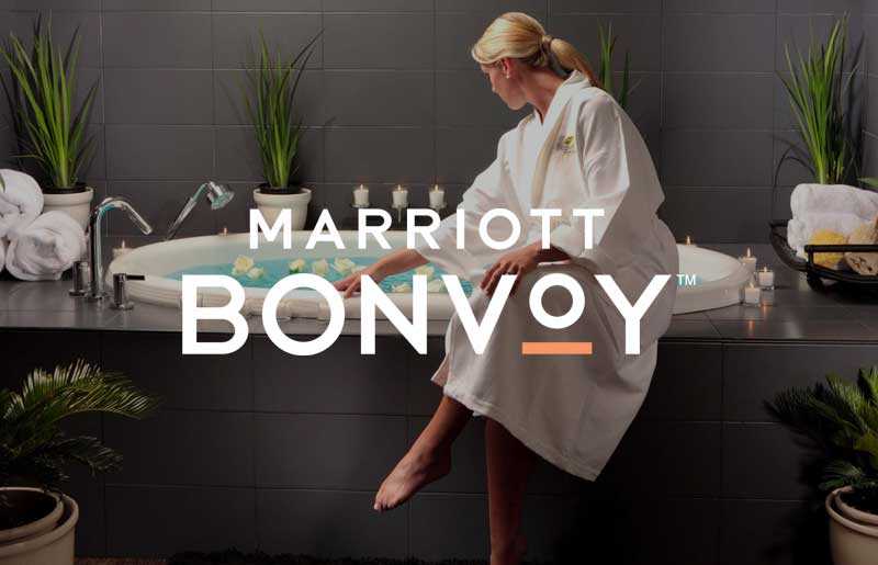 woman in white robe sitting on edge of bathtub with marriott bonvoy logo on top