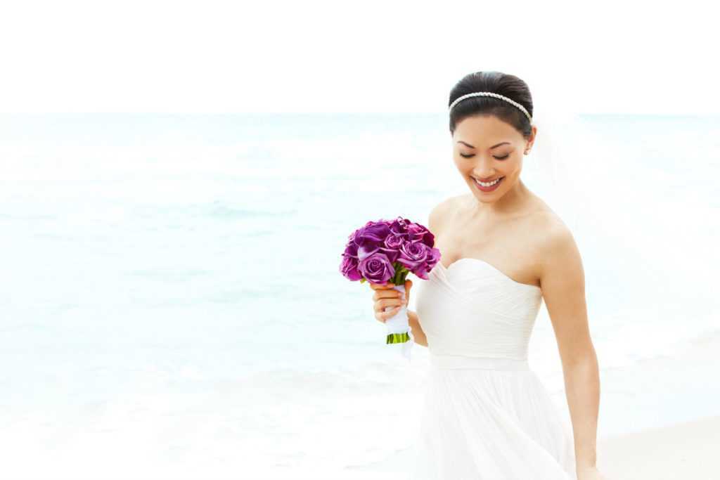 a bride holding a bouquet of flowers on a beach
