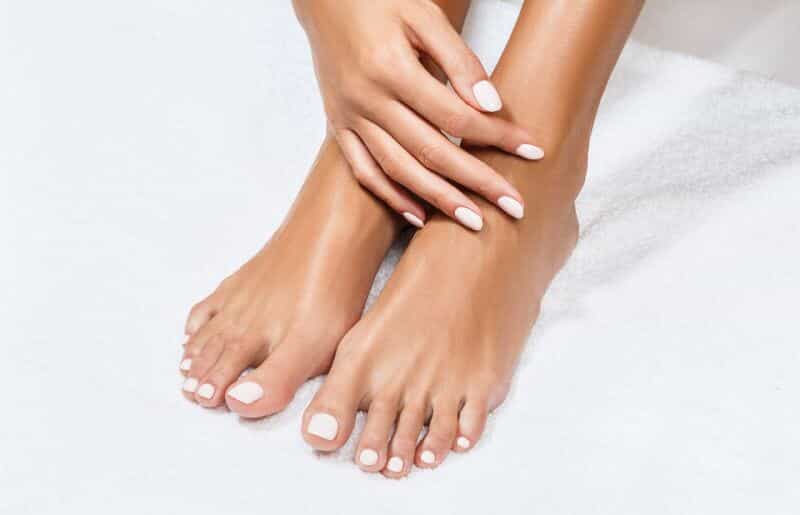 Well-groomed hands resting on freshly pedicured feet.